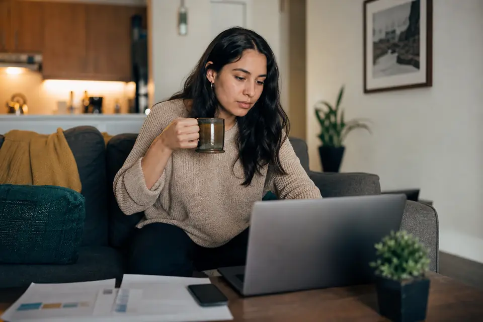 Joven latina compara cuentas de ahorro en su computadora portátil en casa