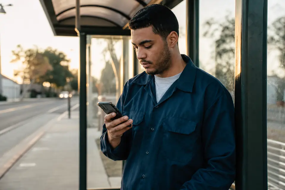 Joven revisa una alerta de saldo bajo en su teléfono en una parada de autobús