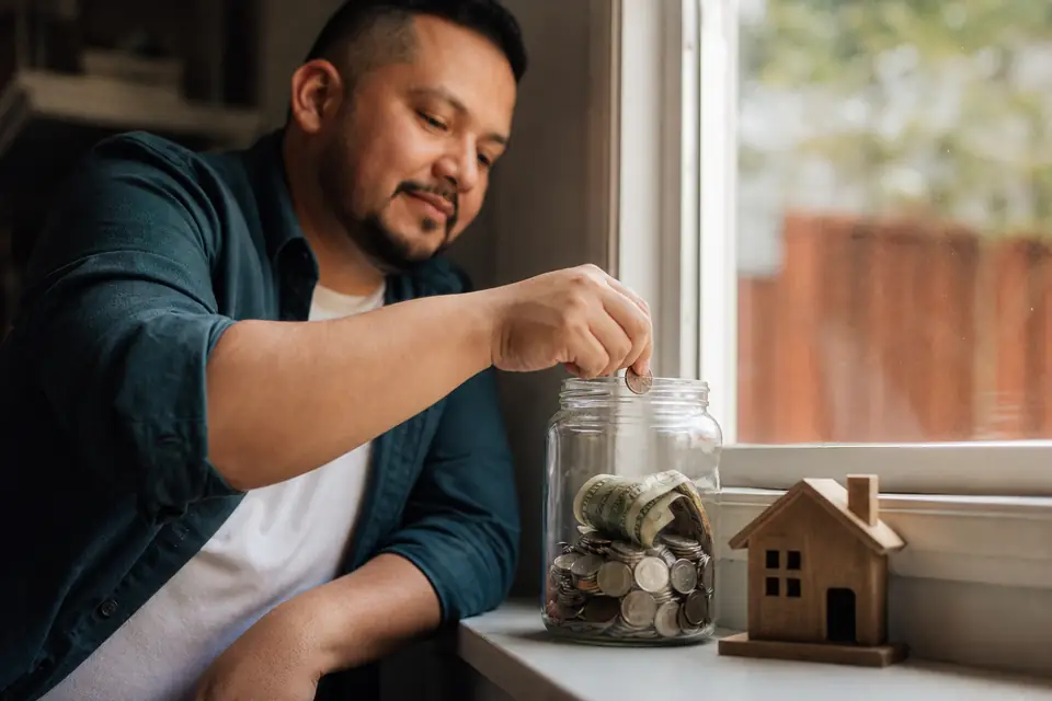 Frasco de ahorros junto a una casita de madera en la ventana