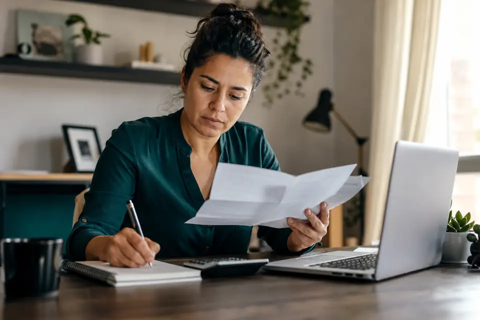 Mujer en oficina en casa comparando dos ofertas de préstamo con calculadora